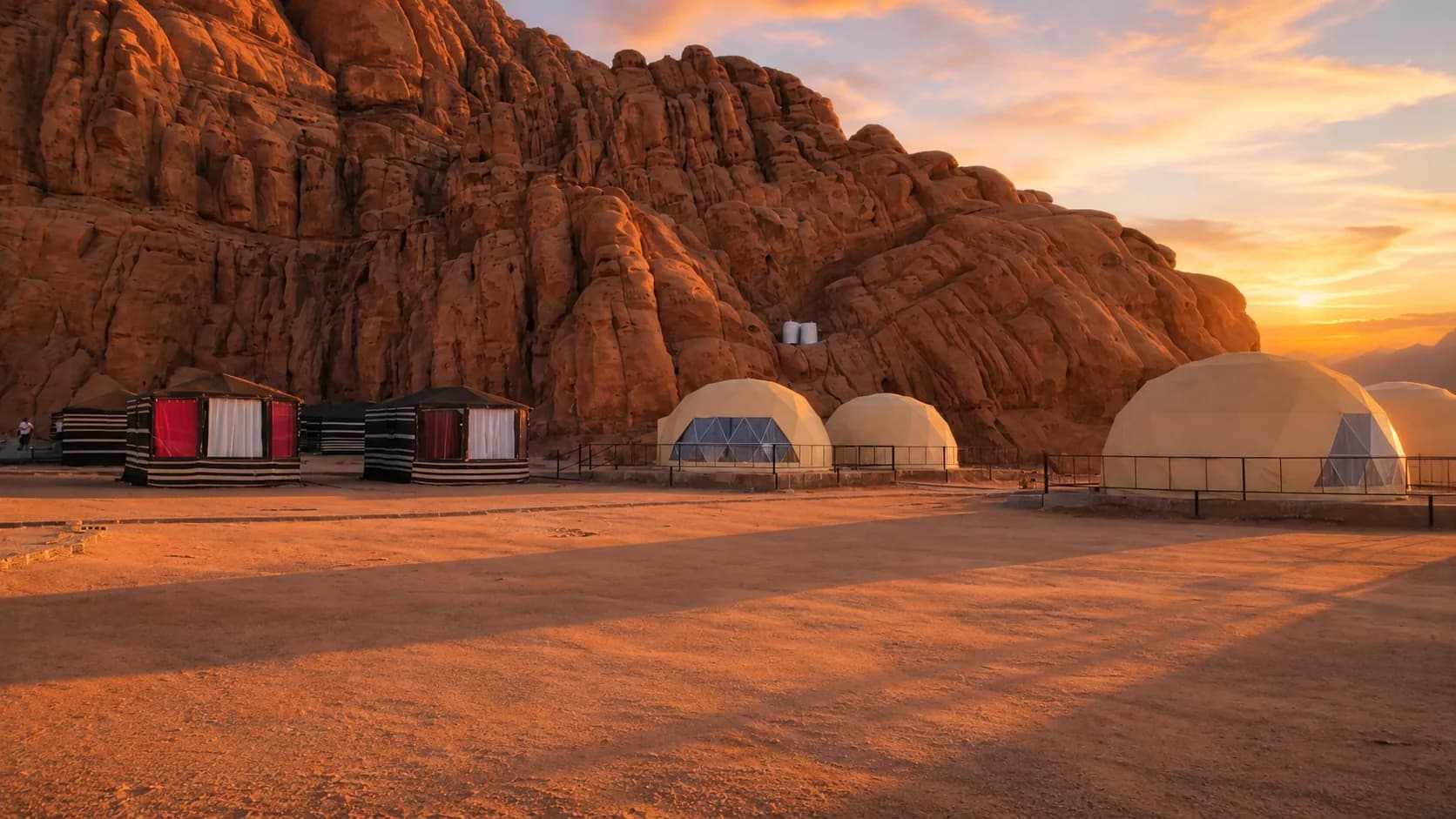 Jamal Rum Camp domes and cabins below Wadi Rum cliffs at sunset.